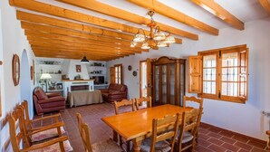 Zona pranzo con tavolo e sedie in legno, cucina sullo sfondo e soffitto in legno con travi a vista.