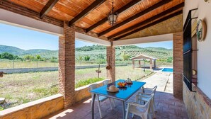 Un portico coperto con un tavolo apparecchiato per mangiare, vista sulla campagna e un piccolo gazebo.
