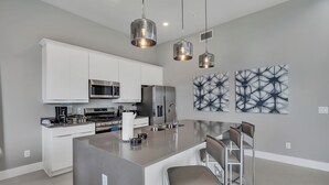 A modern kitchen with white cabinetry, stainless steel appliances, and a central island with bar stools.