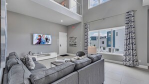 A modern living room with a gray sectional sofa, a flat-screen TV, and a large window with patterned curtains.