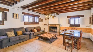 A cozy living room with a fireplace, wooden beams, a sofa set, and a dining table. - Combinación Serval y Pedrizas Montefrío by Ruralidays (Granada)