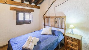 A bedroom with a wooden headboard, a single bed with blue bedding, a nightstand with a lamp, and a window with wooden shutters.