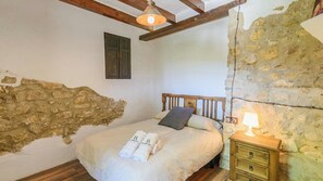 Une chambre avec un mur en pierre, un cadre de lit en bois, une table de chevet avec une lampe et deux serviettes sur le lit.