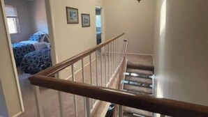 A staircase with a wooden handrail, a ceiling light fixture, and a door leading to another room.