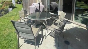 An outdoor patio with a round table and chairs, a yellow umbrella, and a glass door leading to a covered area.