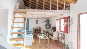 A rustic interior with a wooden staircase, a fireplace, a sofa, a table, and a television. - El Alambique Frigiliana by Ruralidays (Málaga)