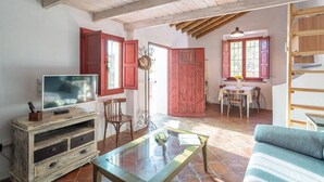 A rustic living room with a television, wooden furniture, a glass coffee table, and a blue sofa. - El Alambique Frigiliana by Ruralidays (Málaga)