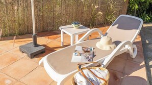 A sunlit outdoor seating area with a lounge chair, a small table, and a basket containing a bag and a hat. - El Alambique Frigiliana by Ruralidays (Málaga)