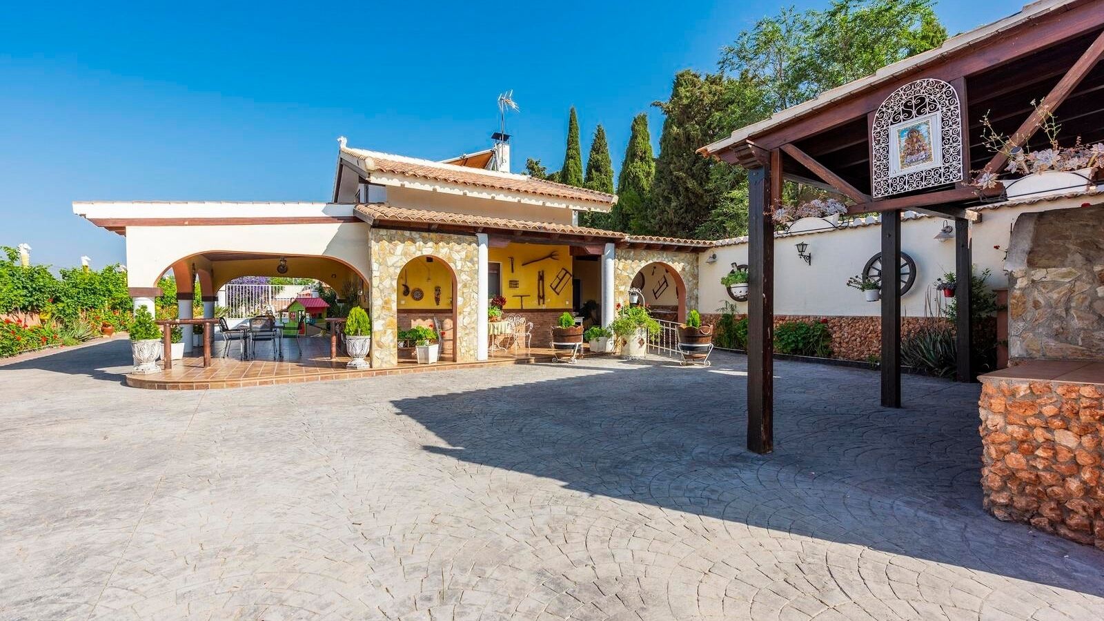 A courtyard with a covered seating area, a stone wall, and a decorative sign.
