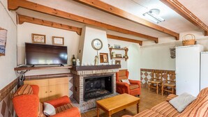 A cozy living room with a fireplace, wooden beams, a television, and a dining area with chairs. - La Estaquilla Dúrcal by Ruralidays (Granada)
