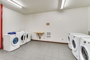 A laundry room with multiple washing machines, a wooden shelf, and a sign indicating laundry services.