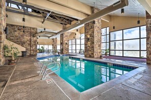 Une piscine intérieure avec des piliers en pierre, de grandes fenêtres et un sol en béton.
