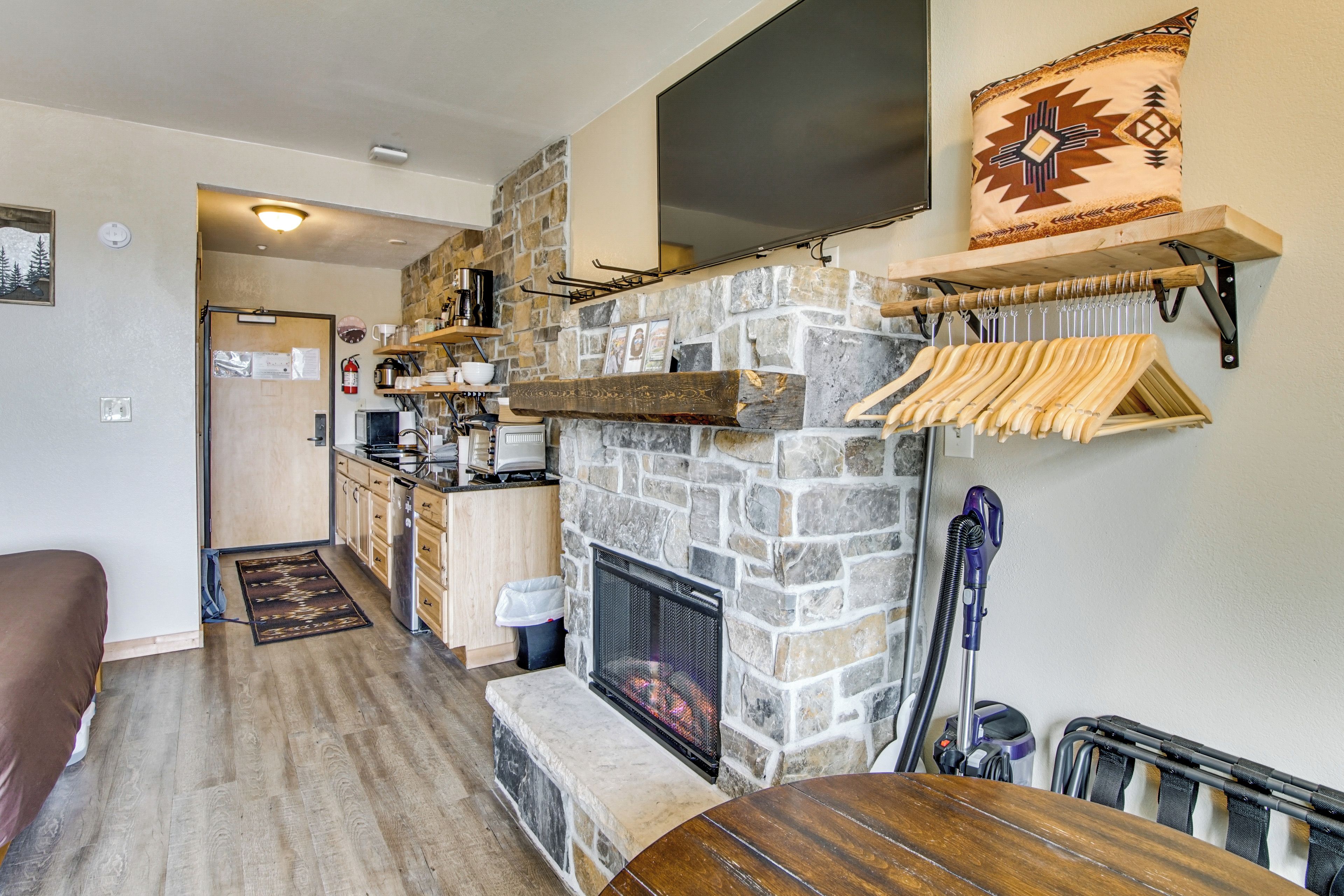 Un salon chaleureux avec une cheminée en pierre, des meubles en bois et une cuisine en arrière-plan.