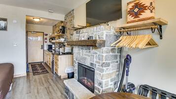 Un salon chaleureux avec une cheminée en pierre, des meubles en bois et une cuisine en arrière-plan.