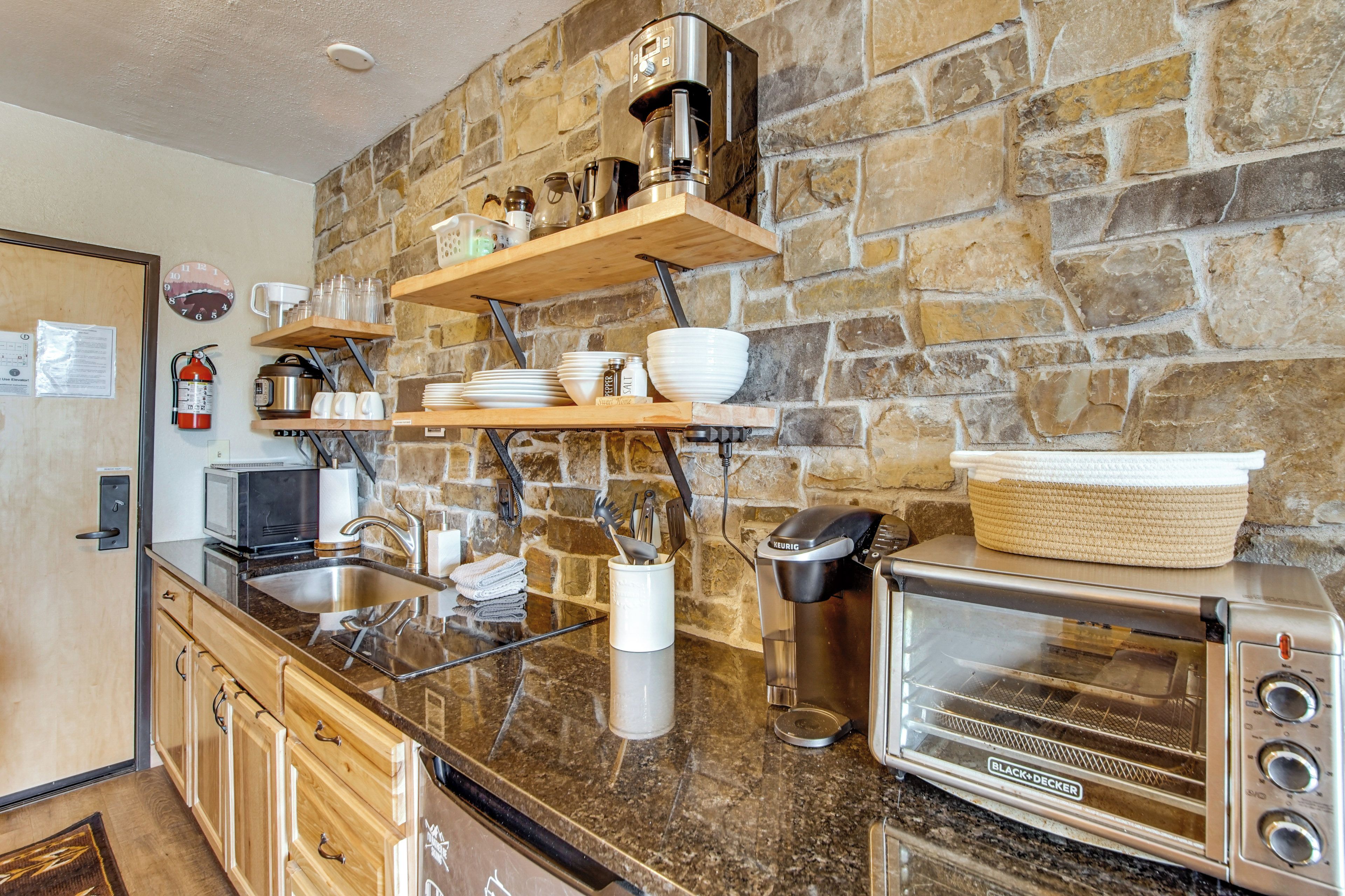 Una cocina con pared de piedra, electrodomésticos de acero inoxidable, estantes de madera y horno tostador.