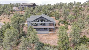 Une maison moderne à deux étages, dotée d’un grand balcon et entourée d’une dense forêt de pins.