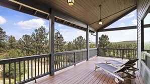 Une terrasse extérieure couverte, dotée d’un plancher en bois, de rampes en métal et de deux chaises longues.