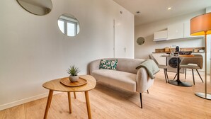 A modern living room with a sofa, a small round table with a plant, and a dining area with chairs and a table. - L'Amandier - Superbe appart au coeur de Lyon 5 (Lyon)
