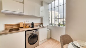 A compact kitchen with a built-in washing machine, a coffee maker, and a window with a view of buildings. - L'Amandier - Superbe appart au coeur de Lyon 5 (Lyon)