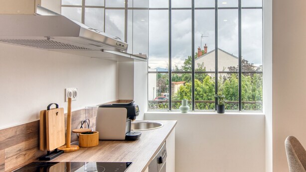 A modern kitchen with a large window, a coffee machine, and a wooden cutting board. - L'Amandier - Superbe appart au coeur de Lyon 5 (Lyon)