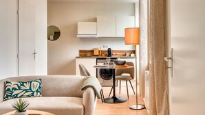 A modern living room with a sofa, a small table with a plant, and a kitchen area in the background. - L'Amandier - Superbe appart au coeur de Lyon 5 (Lyon)