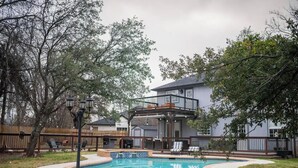 Un pati amb piscina, un pont de fusta i una casa de dos pisos amb un balcó.