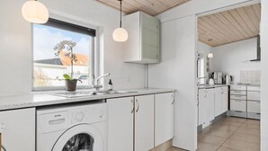 A modern kitchen with white cabinetry, a built-in washing machine, a window with an orchid plant, and pendant lighting. - Lovely home in Blokhus with WiFi (Blokhus)