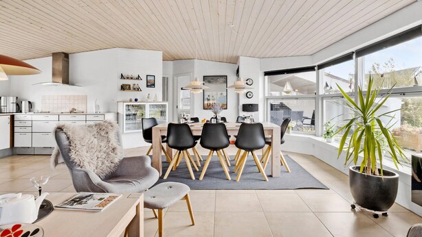 A modern kitchen with white cabinets, a stainless steel range hood, and a dining area with a wooden table and black chairs. - Lovely home in Blokhus with WiFi (Blokhus)