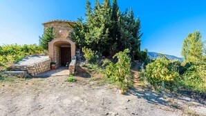 A rustic stone building with a brick archway, surrounded by vineyards and tall trees. - Cortijo El Cerrillo Órgiva by Ruralidays (Granada)