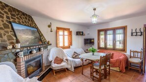 A cozy living room with a fireplace, a stone wall, a television, and a dining area with a table and chairs. - Cortijo El Cerrillo Órgiva by Ruralidays (Granada)
