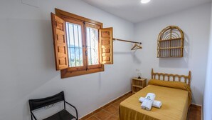 A bedroom with a bed, a window with wooden shutters, a bedside table with a lamp, and a hanging basket. - Cortijo El Cerrillo Órgiva by Ruralidays (Granada)