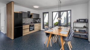 Een moderne keuken met een zwarte koelkast, houten keukenkastjes en een ingebouwde oven. Er is een eethoek met een houten tafel en stoelen, en een groot raam dat voor natuurlijk licht zorgt.