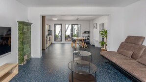 Een moderne woonkamer met een bank, een televisie, een eethoek met een tafel en stoelen, en een keuken die door een open deur zichtbaar is.