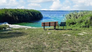 Una panchina e una sedia vicino a un lago, con una zona erbosa e alberi sullo sfondo.