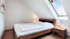 Un letto singolo con poggiatesta in legno in una stanza con soffitto spiovente e finestra a lucernario.