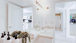 Un baño moderno con lavamanos doble, espejo grande y tocador con artículos de aseo.