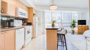 Una cocina moderna con electrodomésticos blancos, una zona de comedor con isla central y un salón con televisor y plantas.