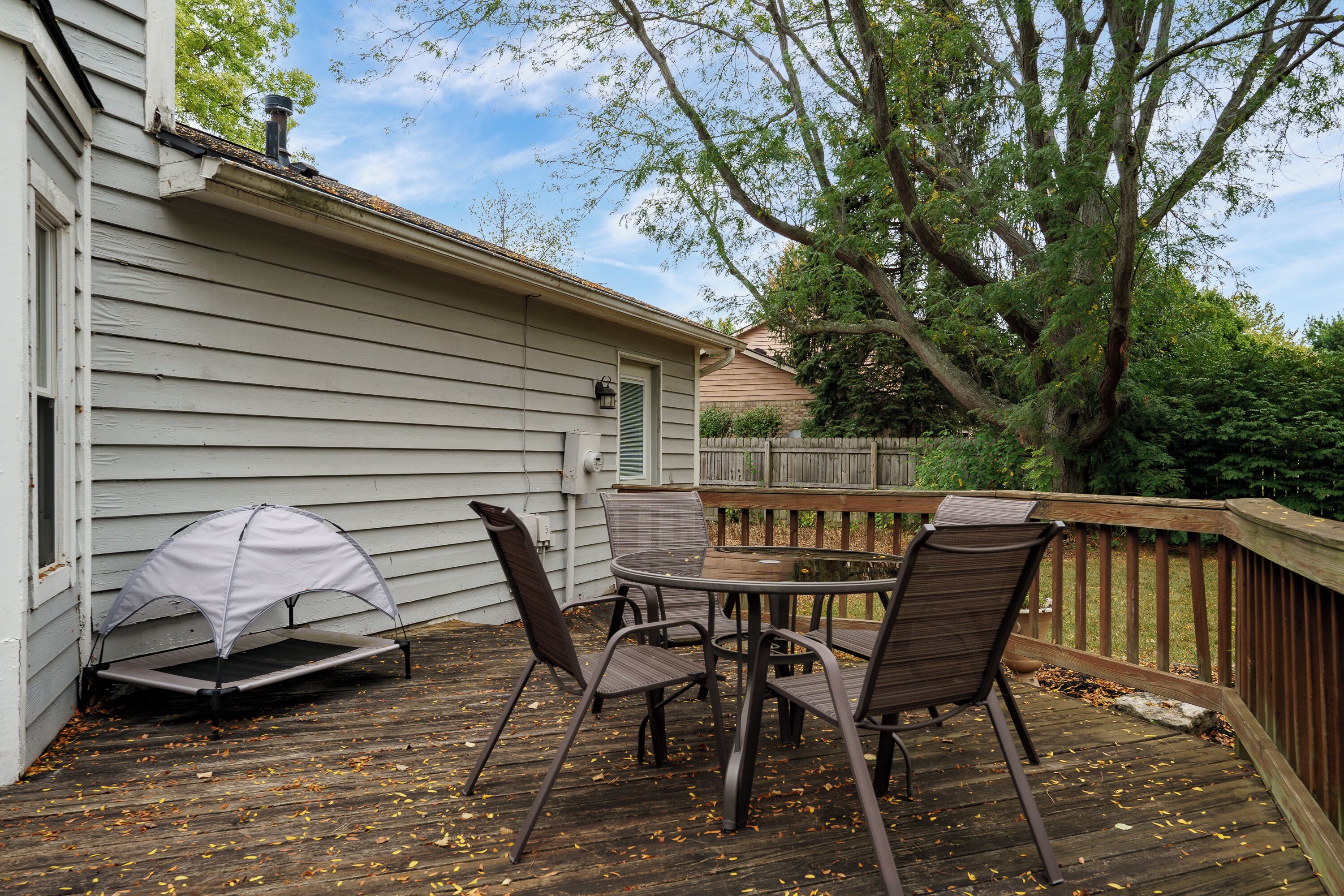 A deck with a table and chairs, a covered grill, and a wooden fence.