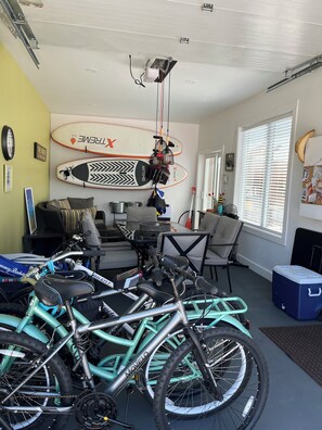Quarto com ventilador de teto, uma prancha de surf, bicicleta e caixa térmica.