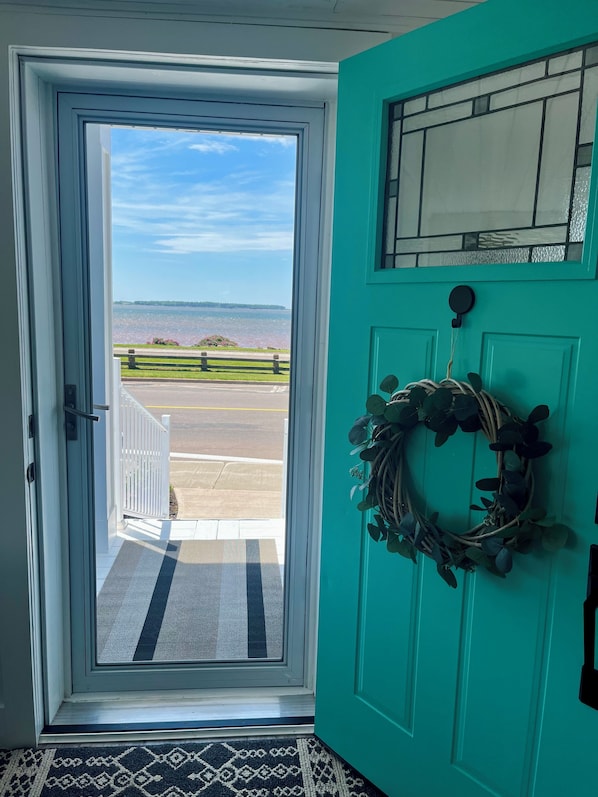 A teal door with a wreath, a view of a body of water, and a white porch railing.