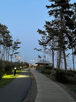 A pathway flanked by trees and a wooden boardwalk, leading to a gazebo-like structure.