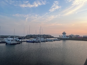 A marina with several boats docked, a lighthouse, and buildings in the background.