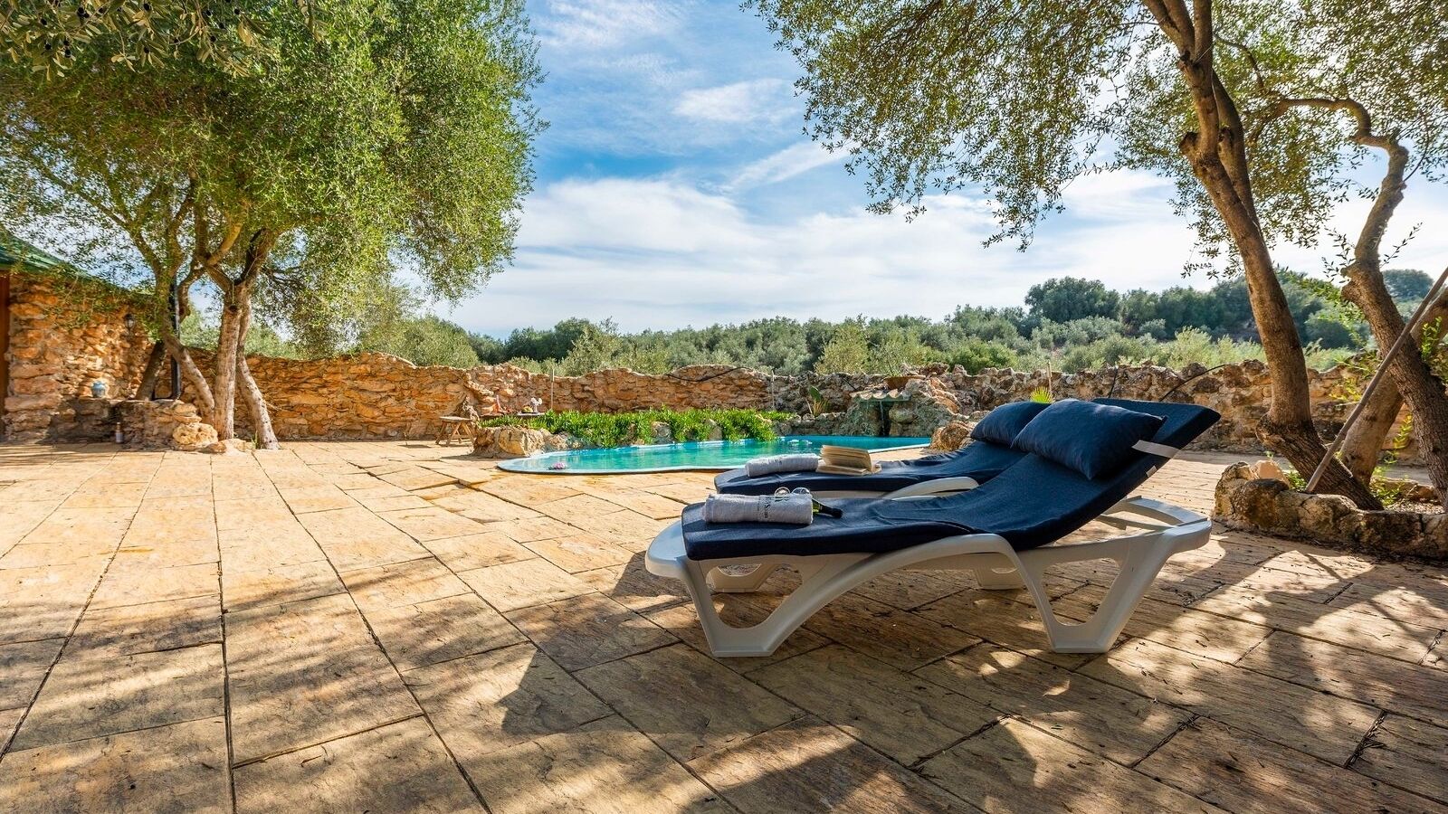 A poolside area with lounge chairs and a stone wall.