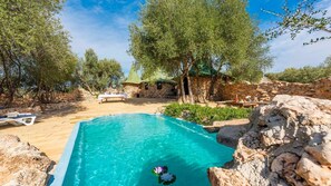 A pool area with clear blue water, surrounded by stone walls and trees.