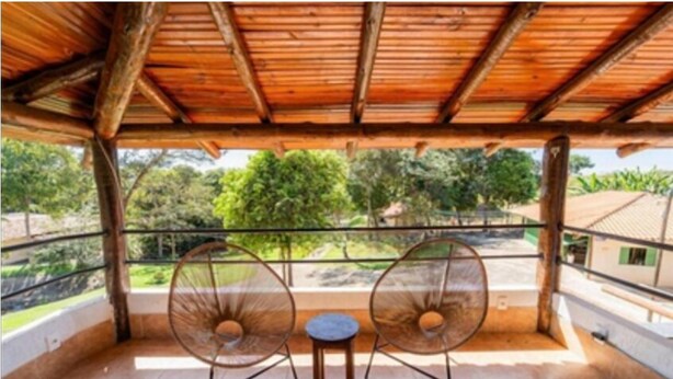 A covered balcony with two chairs and a small table, overlooking a lush green landscape. - Vila do Frade (Alexânia)