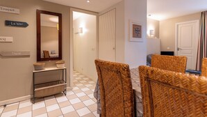 Una camera d'albergo con zona pranzo, caratterizzata da sedie in vimini e un tavolo, uno specchio e cartelli a parete con i nomi delle stanze.