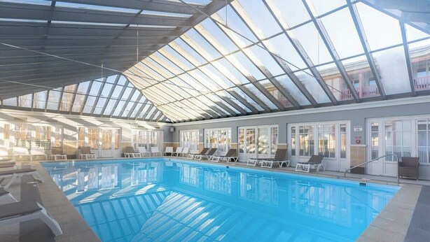 Una piscina interna con soffitti in vetro trasparente, poltrone relax e vista sull'esterno.