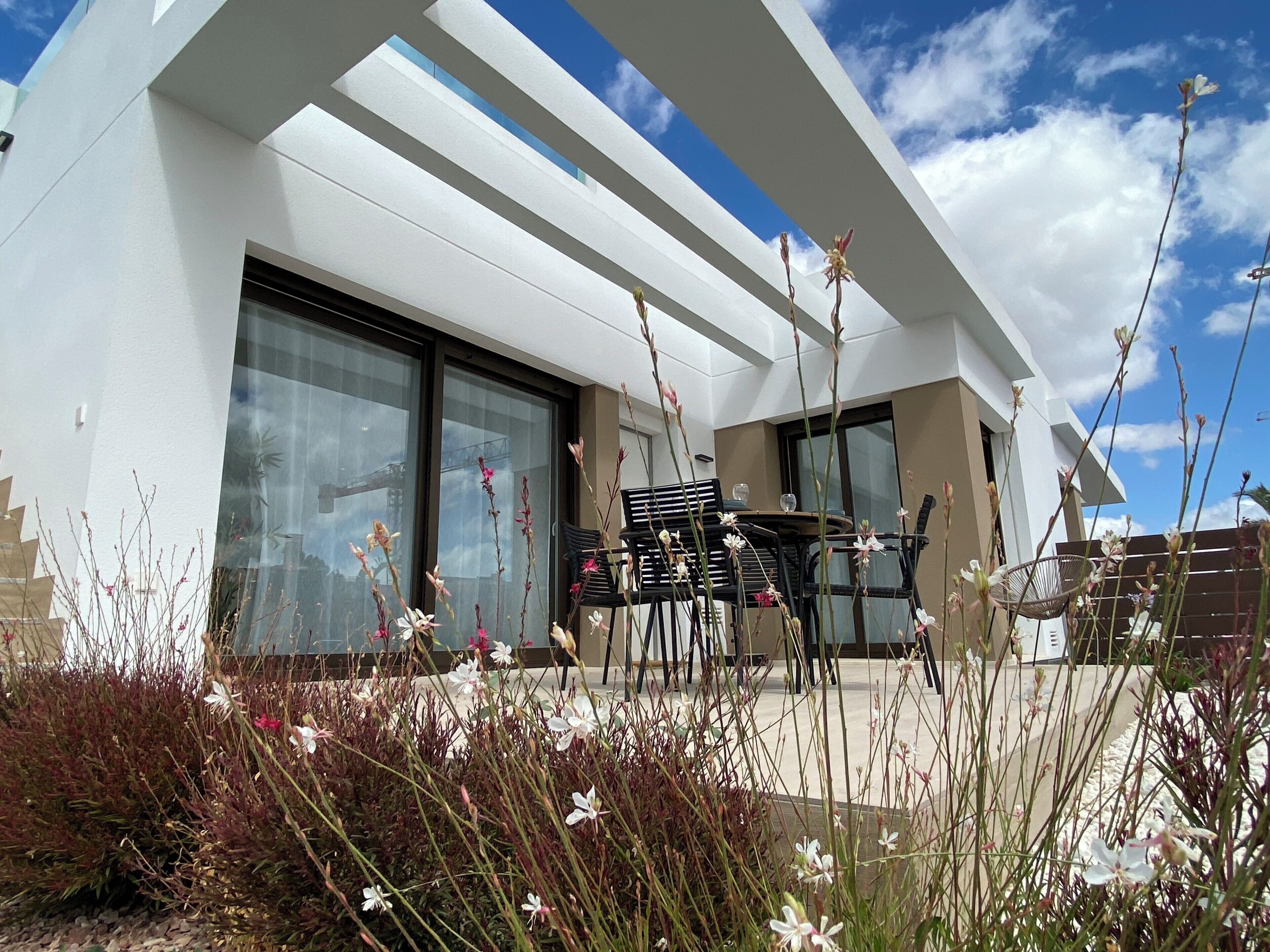 Un bâtiment moderne doté de grandes fenêtres et d’un patio aménagé avec du mobilier d’extérieur.