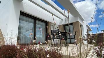 Un bâtiment moderne doté de grandes fenêtres et d’un patio aménagé avec du mobilier d’extérieur.
