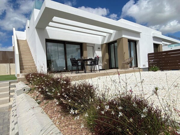 A modern house with a patio, a dining area with chairs and a table, and a staircase leading to the upper floor.